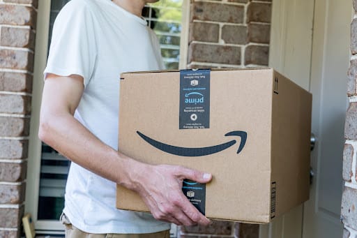 A delivery man carrying an Amazon parcel towards someone’s doorstep