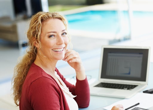A woman smiling in front of the camera while working on her laptop