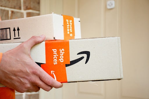  A hand holding Amazon Prime boxes being delivered to the front door of a residence