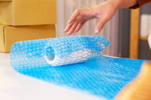 A cropped photo of a woman’s hand packing a vase with a blue bubble wrap.